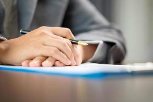 Workplace closeup person professional businesswoman sitting at desk hold pen signing or signature contract paper. Employee woman writing agreement document on paperwork form corporate at work office photo