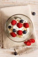 Raspberries, blueberries, cereals and yogurt in a glass bowl on sackcloth and wooden slats. Healthy breakfast for a healthy life. Vertical image view from above. photo