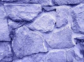 Old stone wall repainted in trendy very peri color of the year 2022. Rough texture. Violet stone background with place for text.