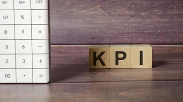 Three wooden cubes with letters KPI , on the wooden table and calculator photo