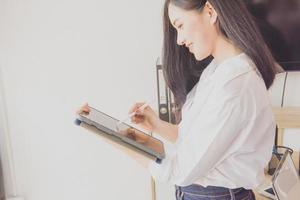 Attractive business women use digital tablets while standing in front of windows in office photo