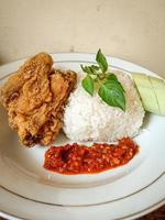 White rice served on a white plate with side dishes of fried chicken, sambal and cucumber photo