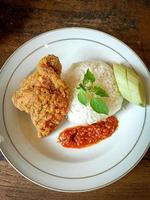 White rice served on a white plate with side dishes of fried chicken, sambal and cucumber photo
