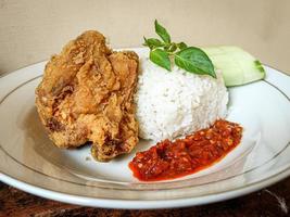 White rice served on a white plate with side dishes of fried chicken, sambal and cucumber photo