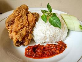 White rice served on a white plate with side dishes of fried chicken, sambal and cucumber photo