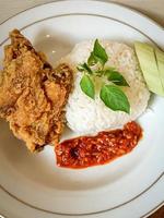 White rice served on a white plate with side dishes of fried chicken, sambal and cucumber photo