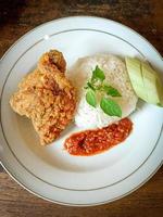 White rice served on a white plate with side dishes of fried chicken, sambal and cucumber photo