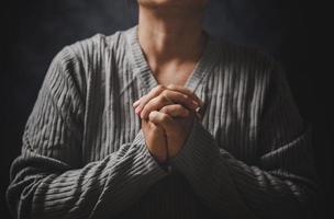 Christ religion and christianity worship or pray concept. Christian catholic woman are praying to god in dark at church. Prayer person hand in black background. Girl believe and faith in jesus christ. photo