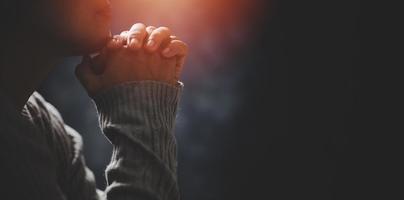 Christ religion and christianity worship or pray concept. Christian catholic woman are praying to god in dark at church. Prayer person hand in black background. Girl believe and faith in jesus christ. photo