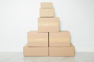 pila de cajas de cartón para mudanzas, habitación vacía con una pared blanca y cajas de cartón con código de barras sin marca en el suelo. entrega de mercancías, compras. cajas de cartón sobre fondo de pared gris. foto