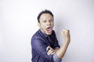 Excited Asian man wearing a navy blue shirt showing strong gesture by lifting his arms and muscles smiling proudly photo