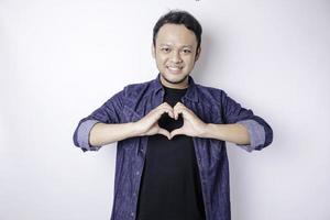 An attractive young Asian man wearing a navy blue shirt feels happy and a romantic shapes heart gesture expresses tender feelings photo
