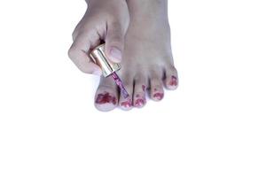 Hand of a little girl paints her toenails with red nail polish isolated on white background. photo
