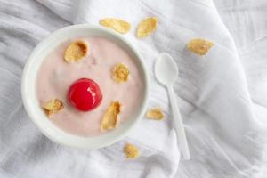 Yogurt, Red Cherry and Dried Corn in white bowl with spoon on white tablecloth. photo