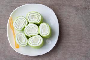 Top view of Young coconut pandan roll cake in white plate on vintage wooden table background. photo