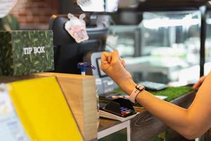 mujer pagando factura a través de smartwatch usando tecnología nfc en café.