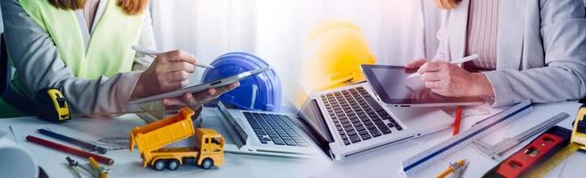 Two colleagues discussing data working and tablet, laptop with on on architectural project at construction site at desk in office photo