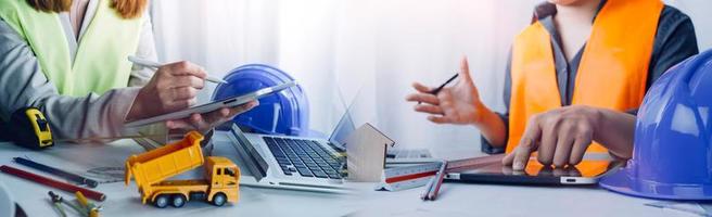 Two colleagues discussing data working and tablet, laptop with on on architectural project at construction site at desk in office photo