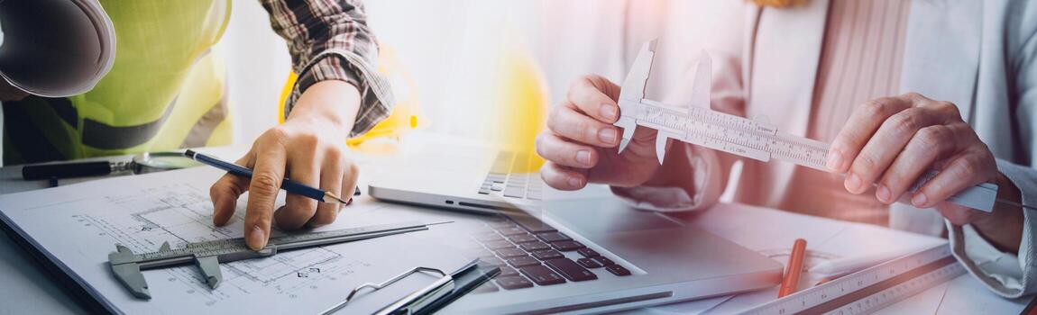 Two colleagues discussing data working and tablet, laptop with on on architectural project at construction site at desk in office photo