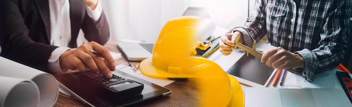 Dos colegas discutiendo el trabajo de datos y una tableta, un portátil con un proyecto arquitectónico en el sitio de construcción en un escritorio en la oficina foto