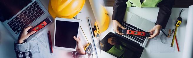 Two colleagues discussing data working and tablet, laptop with on on architectural project at construction site at desk in office photo