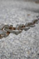 A light gray metal chain made of steel and showing its age is seen up close as it hangs above the broken stone ballast. Selective focus.Vertical view photo