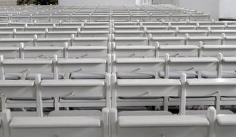 Many empty white benches stand in rows one behind the other as a background photo