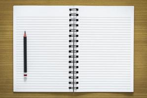 blank spiral notebook and pencil on wood background photo