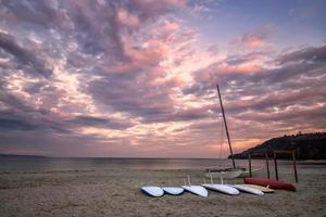 algunas tablas de surf en la playa a la orilla del mar al atardecer con hermosas nubes. fondo de deporte acuático foto