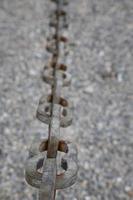 A light gray metal chain made of steel and showing its age is seen up close as it hangs above the broken stone ballast. Selective focus.Vertical view photo