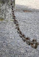 A light gray metal chain made of steel and showing its age is seen up close as it hangs above the broken stone ballast. Selective focus. photo