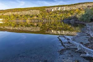 vista asombrosa desde la orilla de un árbol viejo y colinas montañosas con colores otoñales reflejados en el agua del lago foto