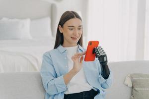 Girl holding smartphone using bionic prosthetic arm at home. Mobile apps for disabled people photo