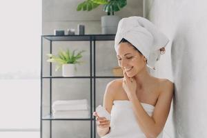 mujer sonriente usando crema hidratante para tratamiento facial en el baño. rutina diaria de cuidado de la piel foto