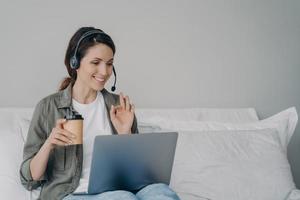 Businesswoman in headset talk by video call on laptop with client showing okay gesture. Remote job photo