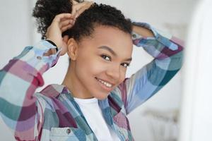 Smiling young mixed race girl holding healthy afro hairs, doing hairstyle. Natural beauty, self care photo