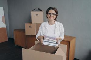 sonriente trabajadora de oficina hispana con gafas empaca cosas en cajas de cartón preparándose para la reubicación foto