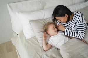 mamá joven acostada en la cama con una hija pequeña después de dormir en el dormitorio. el sueño saludable de los niños foto