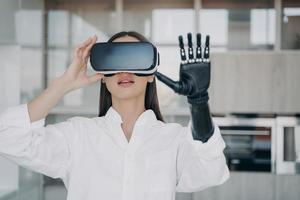 Girl with bionic prosthetic arm wearing virtual reality glasses touch objects in VR by robotic hand photo