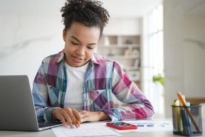 Mixed race girl school student studying at laptop, making homework at home. Distance education photo