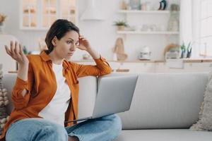 Puzzled woman looking at laptop screen, has problems with computer, virus or bad internet connection photo