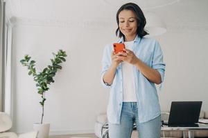 Smiling businesswoman holding smartphone types message in corporate app reads working news in office photo