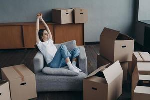 Happy woman rests after packing boxes for moving, dreams about future home. Relocation, first realty photo