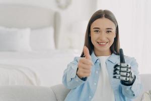 Happy disabled girl with prosthetic arm, showing thumb up gesture, recommends bionic hand prosthesis photo