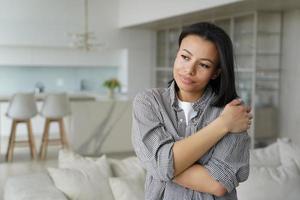 Calm happy female embraces herself feeling self love, self-pride, dreaming, standing at cozy home photo