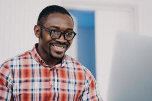 Smiling african american man in glasses working online at laptop, reading email with good news photo