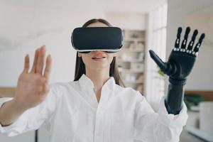 Disabled girl in virtual reality glasses touches objects training to use bionic prosthetic arm photo