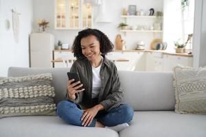 African american teen girl use modern phone apps chatting in social network, shopping online at home photo