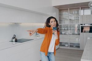 Energetic girl listens to music, singing using smartphone as mic at home. Musical mobile apps ad photo