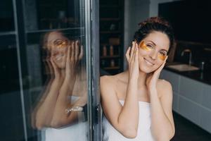 hermosa mujer con parches de hidrogel hidratantes debajo de los ojos haciendo el procedimiento de cuidado de la piel después de la ducha foto